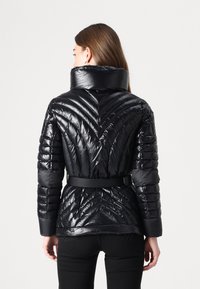 Giacca a vento nera con colletto alto, vita cintata e design a rombi. Realizzata in materiale lucido con maniche lunghe e aderenti.