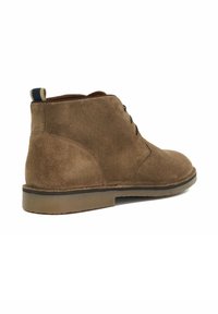 Brown suede chukka boots with a smooth texture, round toe, and stacked rubber sole. Features black laces and a navy heel loop.