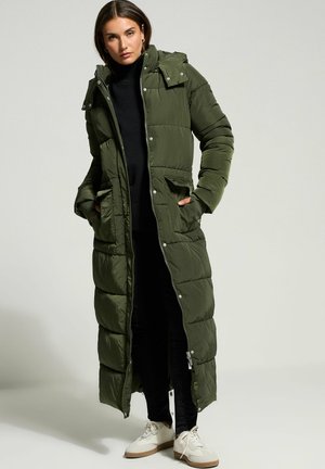 Lange, olijfgroene onweersjas van nylon met een rits- en drukknoopsluiting, voorzien van twee zijzakken en een afneembare capuchon.