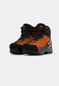 Un paio di scarponi da trekking alti arancioni e neri, con suole robusta e lacci multicolori, posizionati affiancati su uno sfondo bianco.