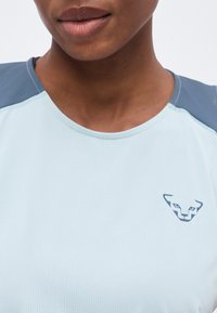 Gros plan d'une personne portant un maillot de sport bleu clair avec un logo panthère bleu foncé sur la poitrine et des panneaux d'épaule bleu plus foncé.