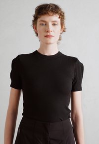 Camiseta negra de canalé con mangas cortas, presenta un escote redondo y un diseño ajustado. Textura suave, silueta ceñida.