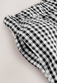 Schwarz-weißes Vichy-Karosgewebe mit einer strukturierten Haptik, das Falten und eine weiche, leicht zerknitterte Optik nahe dem Rand aufweist.