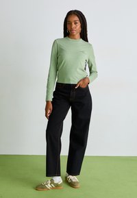 Ανοιχτό πράσινο μακρυμάνικο μπλουζάκι με εφαρμοστή γραμμή, μαύρο ψηλόμεσο παντελόνι και πράσινα αθλητικά παπούτσια με λευκές λεπτομέρειες.