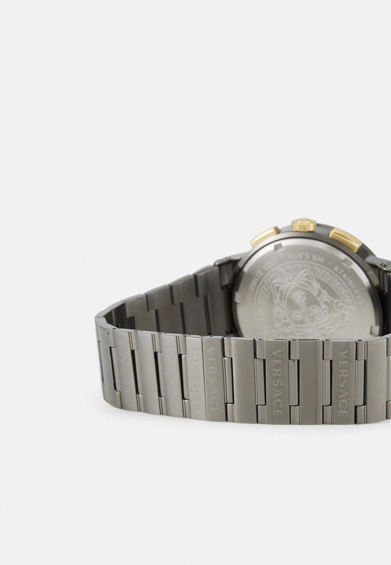 Edelstahlarmbanduhr mit grauem Armband, ausgestattet mit einem silberfarbenen Gehäuseboden und goldenen Akzenten an der Krone. Strukturierten Glieder mit eingraviertem "Versace".