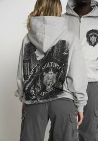 Hellgrauer Hoodie mit einem grafischen Druck eines brüllenden Leoparden und dem Wort "MULTIPLY" auf der Rückseite; aus weichem Material, lockere Passform.