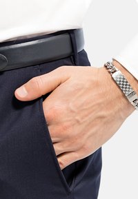 Pantaloni blu navy con tasca laterale, una cintura in pelle nera liscia e un braccialetto argentato con un design testurizzato e chiusura.