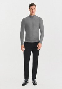 Szary sweter z golfem, wykonany z miękkiego materiału, o dopasowanym kroju; zestawiony z czarnymi spodniami slim-fit i czarnymi botkami za kostkę. Gładkie tło.
