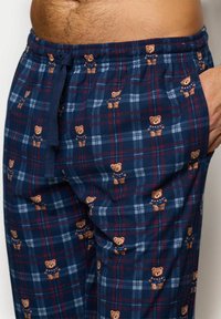 Granatowe w kratę spodnie piżamowe z wzorem niedźwiedzi i czerwonymi akcentami. Wykonane z miękkiego materiału, z elastycznym paskiem i detalem w postaci sznurków.
