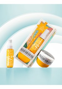 Imballaggio giallo con un flacone spray e un barattolo di crema. Scatola decorativa con un motivo a scaglie colorate; etichette chiare con i dettagli del prodotto.