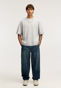 Šedé oversized tričko, volné modré džíny a béžové tenisky. Tento outfit má ležérní design s uvolněným střihem.