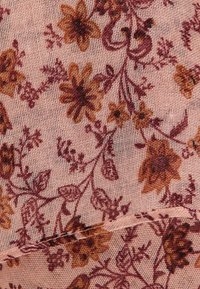 Tissu à motif floral avec un fond rose, présentant des fleurs et des feuilles marron foncé. La texture est douce et légèrement transparente, adaptée à l'habillement.