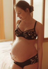 Set di lingerie nero, caratterizzato da un delicato motivo in pizzo con accenti dorati, tessuto trasparente e design aderente, indossato da una persona in gravidanza.