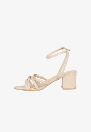 Sandal beige con tacco a blocco, caratterizzato da più cinturini incrociati e una cinghia alla caviglia. Texture liscia con dettagli dorati.