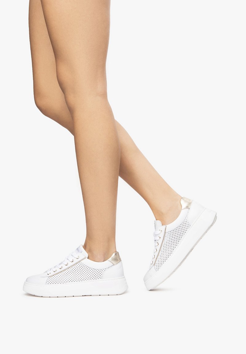 Zapatilla blanca con parte superior perforada y detalles dorados. Cuenta con cordones planos y una suela blanca gruesa. Parece ligera y casual.