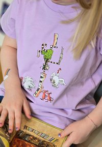 Liila t-paita, jossa on leikkisä printti raidallisesta kissasta vihreässä villapaidassa, kahdesta kanasta ja kahdesta sarjakuvamaisesta ruskeasta koirasta.