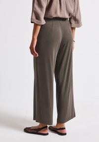 Pantalon large vert olive en tissu doux, avec une taille haute et des ourlets fendus, associé à des sandales en mesh noires.