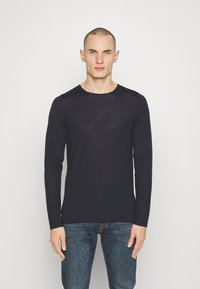 Maglietta a maniche lunghe nera realizzata in un tessuto morbido, con scollo rotondo e vestibilità slim, abbinata a jeans in denim blu.