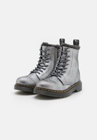 Metallische zilveren enkelboots met een gebarsten textuur, zwarte veters, nepbontvoering en gele stiksels langs de zwarte zool.