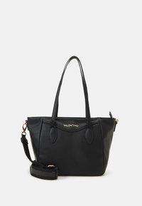 Svart läder tote-väska med en grynig textur, dubbla axelremmar och en avtagbar rem. Har en guldfärgad logotyp och en strukturerad form.