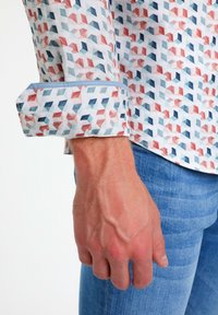 Daudzkrāsains ģeometrisks raksts uz krekla ar gaiši zilu aproci, izgatavots no mīksta auduma. Nēsāts kopā ar gaiši ziliem džinsiem.