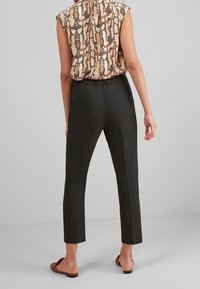 Czarne dopasowane spodnie o długości 7/8, o gładkiej fakturze i dwóch tylnych kieszeniach. Noszone z beżową bluzką w wzory.