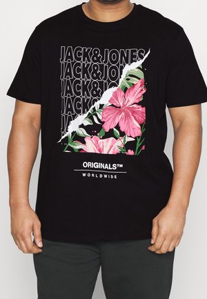 Mand iført en sort t-shirt med gentagen tekst "JACK & JONES", revne effekt der afslører pink hibiscus blomster og "ORIGINALS™ WORLDWIDE" nedenunder.