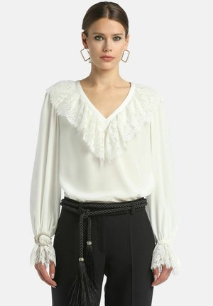 Witte blouse met een kant afgewerkte kraag en kantdetails bij de manchet. Lange mouwen, V-hals ontwerp, gecombineerd met zwarte hoge taille broeken.