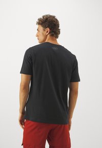 Svart t-skjorte med kort erm og rund hals, med logodetaljer på baksiden, parret med røde shorts. Glatt stoff, avslappet passform.