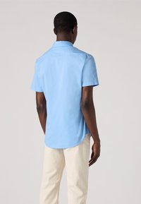 Lichtblauw shirt met korte mouwen van katoen, met een rugpas en een gebogen zoom, gecombineerd met crèmekleurige broeken.