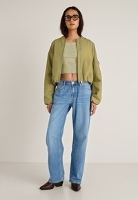 Zelena bomber jakna s elastičnim manžetama, svijetlosiva rebrasta kratka majica, plave traperice širokih nogavica i smeđe gležnjače s petom.