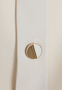 Détail d'un bouton sur un tissu beige doux. Le bouton rond présente un design divisé : moitié blanc brillant et moitié or texturé.