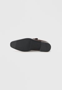 Suela de zapato de cuero con una parte inferior de goma negra texturizada, forma cónica y ranuras sutiles para tracción. Presenta un diseño de tacón curvado.