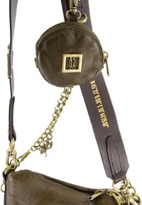 Kleine ronde olijfgroene leren pouch met het AS98-logo bevestigd aan een donkerbruine leren band met gouden ketting en coördinaten in gouden letters.