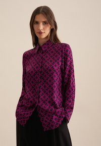Camicia a maniche lunghe in magenta lucido con motivo nero, caratterizzata da disegni circolari, colletto classico e chiusura con bottoni.