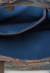 Innenansicht einer mit Blumenmuster versehenen Tasche mit blau-black gestreiftem Futter und einer großen offenen Tasche mit braunen Lederakzenten.