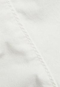 Gros plan sur un tissu blanc avec une couture diagonale et une texture de points de couture visibles.