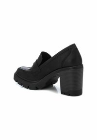 Zapatos de tacón platforms negros con puntera redondeada, parte superior de cuero liso, tacón robusto acanalado y suela gruesa de goma. La vista lateral muestra detalles de costura.