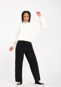 Hvid sweatshirt med løs pasform og ribbede manchetter, parret med højhalsede sorte jeans og sorte sneakers med hvide såler.