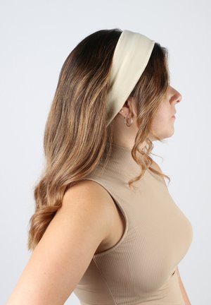 Fascia per capelli in tessuto beige indossata su capelli castani e ondulati. Texture liscia con un design solido, enfatizza il profilo dell'utente.