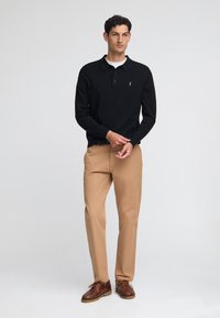Svart långärmad polo med krage, beige chinos och bruna snörskor. Minimalistisk logotyp på skjortan. Slät tygstruktur.