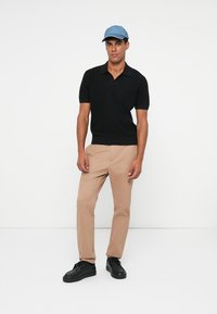 Černý polo triko s krátkým rukávem, béžové chinos kalhoty a černé tenisky. Celý outfit dotváří světle modrá čepice s logem na polo.