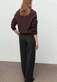 Suéter de punto marrón con un corte relajado, combinado con pantalones de pierna ancha de cintura alta en negro. Textura suave, diseño minimalista.