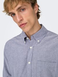 Lichtblauw overhemd met knopen van textuurstof en een borstzak. Heeft een button-down kraag en witte knopen.