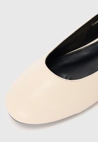 Chaussure plate en cuir beige à bout arrondi et doublure intérieure noire sur fond blanc uni.