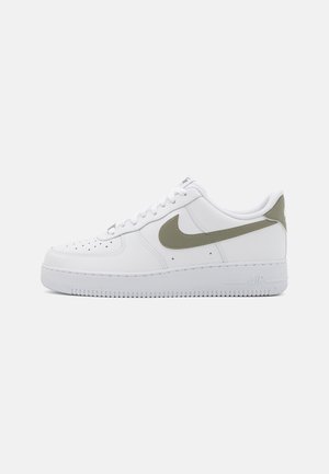 White low-top sneaker with olive green Nike swoosh, perforated toe, laces, and thick sole on plain light background.