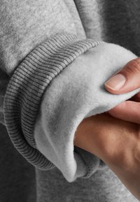 Sivi rukav sweatshirt-a s rebrastim dizajnom, s mekanim, flis unutarnjim podstavljanjem i glatkim materijalom na vanjskoj površini.