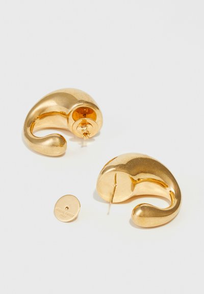 Boucles d'oreilles en métal doré présentant un design abstrait et incurvé. Comprend un fermoir à tige pour un maintien sécurisé, avec un petit logo en relief sur un support circulaire.