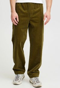 Olive green corduroy pants with a straight cut, featuring a textured surface and elastic waistband. Paired with light gray athletic shoes.