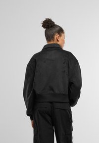 Jacheta bomber din suede negru, cu guler, manșete și tiv elastic. Prezintă un design simplu, o textură moale și o croială lejeră.